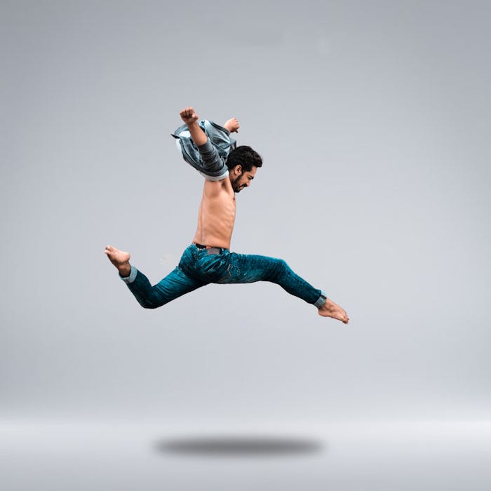 A male dancer shows his agility with a powerful leap captured in a studio setting.